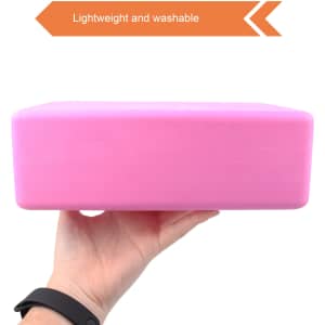 A pink EVA yoga block held in a hand, featuring a smooth surface and lightweight design.