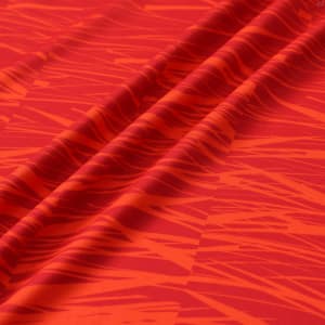A red hooded sports jumper featuring a bold, textured pattern with shades of orange and darker red. The fabric includes a logo.