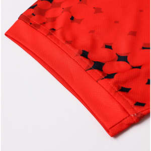 A close-up of a red football jersey featuring a patterned design and a logo. The fabric is 100% polyester.