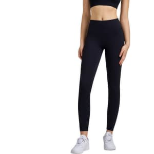 High-waisted black LYCRA yoga leggings displayed on a model, complemented by a black crop top and white sneakers.