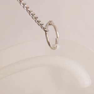 A clear, flexible sign holder with a silver metal hook attached to a chain.