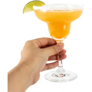 A margarita glass filled with orange drink, garnished with a lime wedge and salt on the rim. Hand holding the glass.