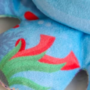 A blue keyring featuring a plush animal design with colourful patterns of red and green elements.