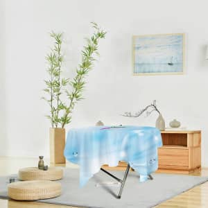 A round table cover featuring a blue design, placed on a folding table in a bright, minimalist room.
