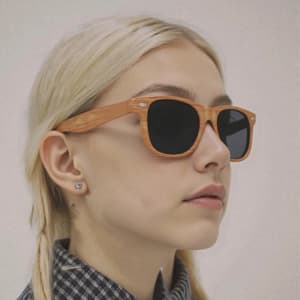 Wooden sunglasses with a light brown frame and dark lenses worn by a person with blonde hair.