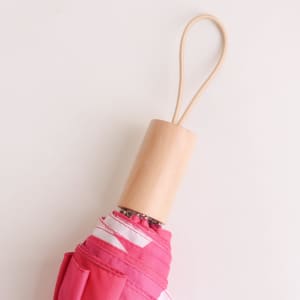 A lightweight pink umbrella with a wooden handle and a loop for hanging. It also features a logo.