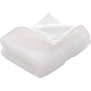 A folded white embroidered cotton hand towel sits on a flat surface. The towel has a soft texture and features a logo.