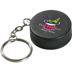 A black hockey puck stress reliever attached to a metal keyring, featuring a logo on the surface.