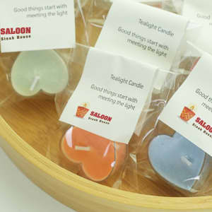 Tealight candles in various pastel colours, packaged in clear bags, arranged in a wooden bowl.