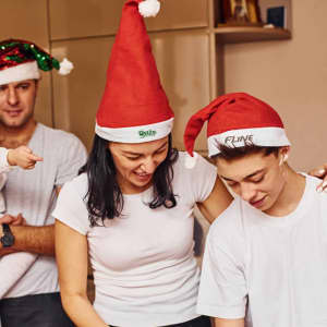 Three individuals wearing red Santa hats with white trim, engaging in a festive activity. One hat features a logo.
