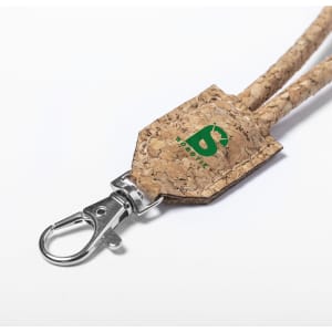 A cork lanyard featuring a metal clasp and a small branded tag in green. The natural cork texture is prominently displayed.