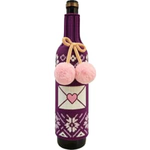 A drink bottle inside a purple custom knitted sleeve, featuring pink pom-poms and a heart design.
