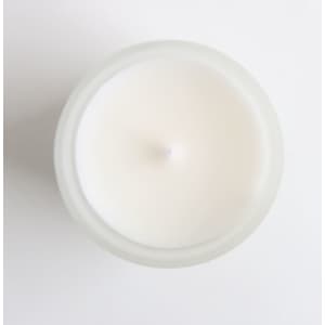 A white glass candle in a frosted container, viewed from above, with a simple design and no visible branding.