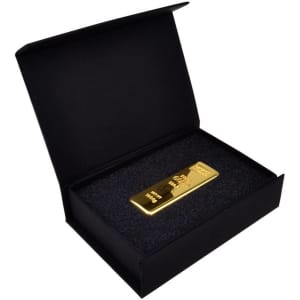 A black magnetic gift box contains a gold bar resting on black foam. The box features a subtle branding logo.
