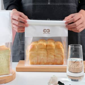 A person holds a clear, resealable bag containing sliced bread. The bag features a logo at the top.