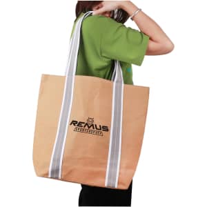 A person carrying a small, washable kraft paper bag with grey cotton handles. The bag is light brown and features a logo.