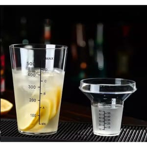A drink bottle and measuring cup with markings, featuring clear plastic and a spout, alongside sliced lemons.