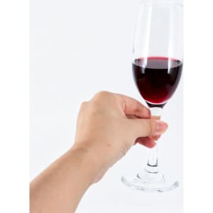 A hand holding a clear, stemmed wine glass filled with red wine against a white background.