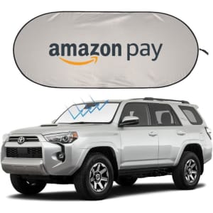 A silver SUV parked with a grey car sunshade featuring a logo, positioned on its windshield.