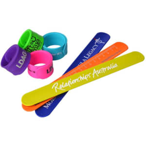 A collection of silicone snap wristbands in various colours, including purple, blue, green, and yellow, with a ruler.