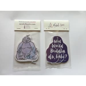 Two air fresheners featuring a Buddha design, one in a purple colour and the other in white, each with a header card.
