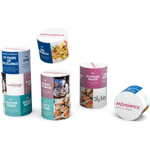 Various cylindrical promotional containers in vibrant colours, featuring images of food and a logo on each.