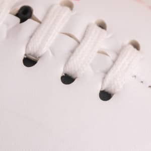 A close-up of a white mini footy ball showing laces and stitching details. There is a logo on the surface.