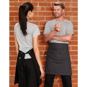 A grey canvas short waist apron featuring a tie-back, displayed against a brick wall backdrop.