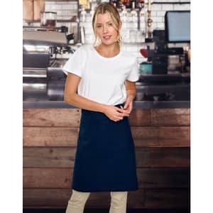 A woman wearing a navy canvas short waist apron over a white t-shirt, standing in a café setting.