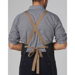 A denim bib apron with a cross-back design and a brown tie, worn by a person in a checked shirt.