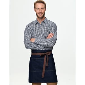 A man in a checkered shirt wears a denim half apron with a brown tie belt. The apron features pockets and a logo.