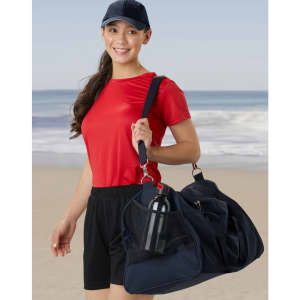 A woman in a red shirt and black shorts carries a navy blue duffle bag with a drink bottle visible in the side pocket.