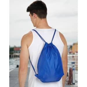 A blue swim backpack with drawstring closure, worn on the back of a person, showing a scenic waterfront.