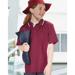 A girl in a maroon polo shirt and a red hat holds a navy blue jacket, smiling in an indoor setting.