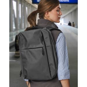 A grey backpack worn on the back of a person, set in a blurred airport environment. It features a logo.