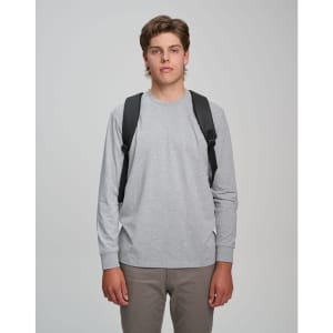 A model wearing a grey long-sleeve shirt and khaki pants, showcasing a black backpack on both shoulders.