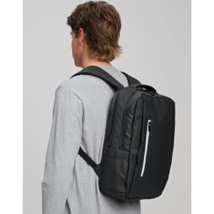 A black backpack with multiple compartments is worn on the back of a person in a grey top. The backpack features a logo.