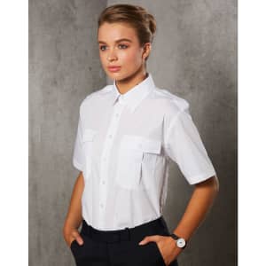 A white short sleeve button-up shirt with two chest pockets, modelled by a woman against a textured background.