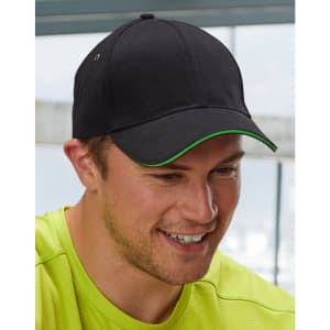 A black cap with a green peak, featuring a logo, worn by a smiling man in a bright yellow shirt.