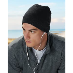 Acrylic knitted marl beanie in dark grey worn by a model with earbuds, set against a coastal background.