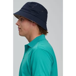 A contrasting underbrim bucket hat in navy, worn by a person in a teal polo shirt, featuring ventilation eyelets.