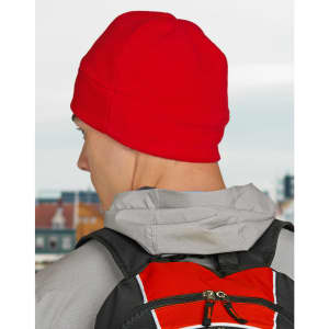 A red fleece beanie worn by a person with a grey hoodie and a black backpack. The background features a cityscape.