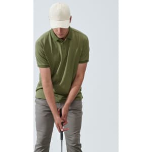 A light beige unstructured cotton twill cap worn by a person in a green polo and grey pants, indoors.