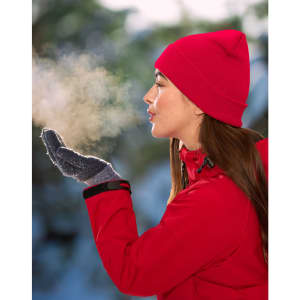 A woman in a bright red beanie and gloves exhales visibly in a snowy outdoor setting.