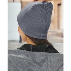 A grey cable knit beanie, viewed from the back, worn by a person in a jacket outdoors.