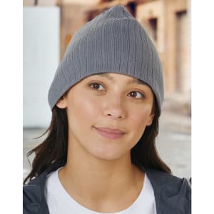 A grey cable knit beanie worn by a woman with long hair, set against a blurred urban background.