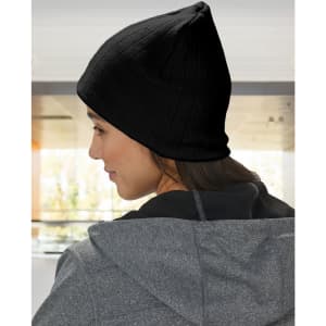 A beige cable knit beanie with a fleece headband, worn on a person’s head, seen from the side.