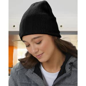A cable knit beanie in a soft beige colour, worn by a woman with a fleece headband underneath.