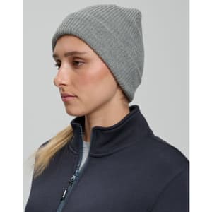 A grey roll-up cable knit snug beanie displayed on a model, wearing a dark jacket. The beanie has a logo.