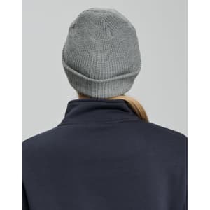 A grey cable knit beanie with a rolled cuff, seen from the back, worn by a person in a navy top.